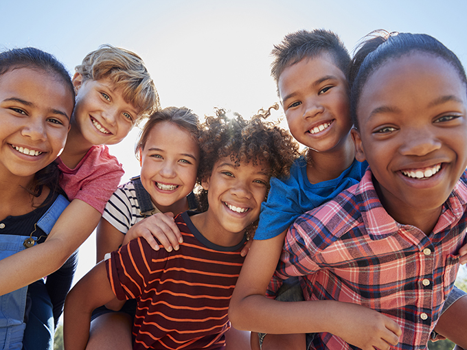 six pre-teen friends piggybacking in a park, close up portrait